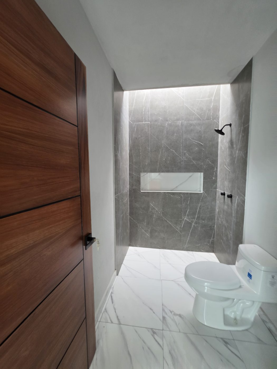 Baño completo con muro tipo mármol gris, nicho y regadera negra